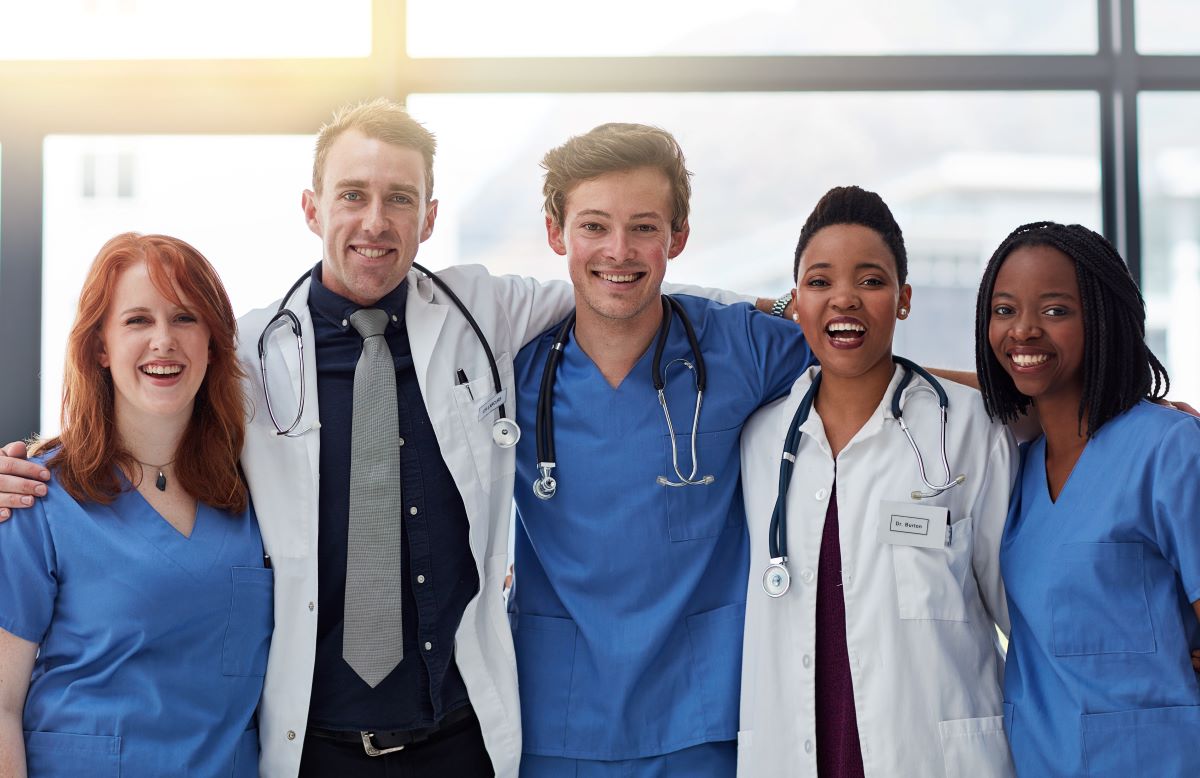A group of nurses and physicians embrace and smile for the camera.
