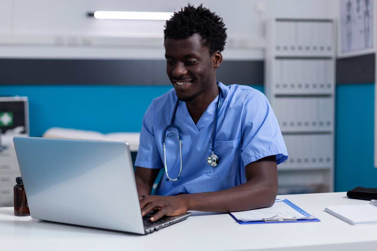 African-American male nurse in scrubs typing out a nursing care plan for dementia on laptop.