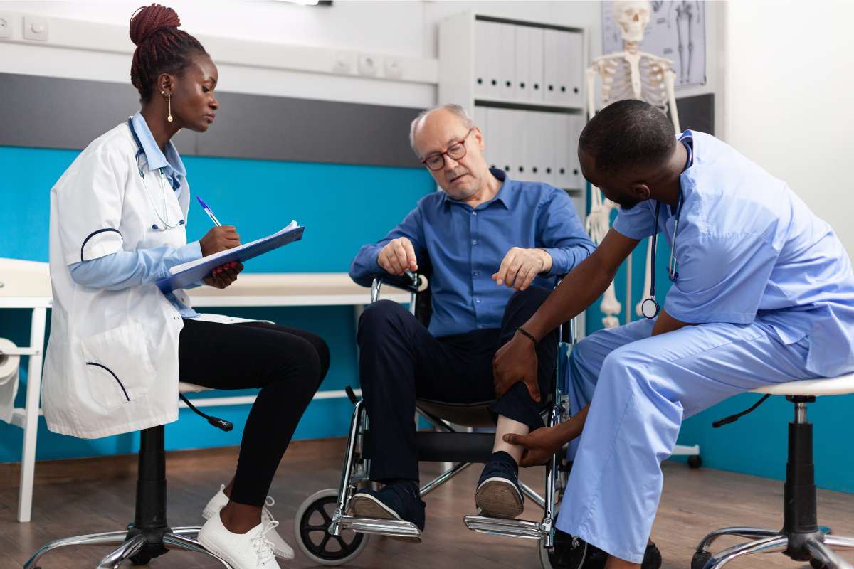 Man nurse checking injured knee leg of sick retired senior patient while therapist doctor writing medical expertise on clipboard during clinical examination in hospital office.