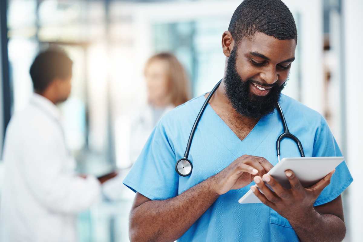 Young male nurse with beard reading about nursing theories on a tablet.