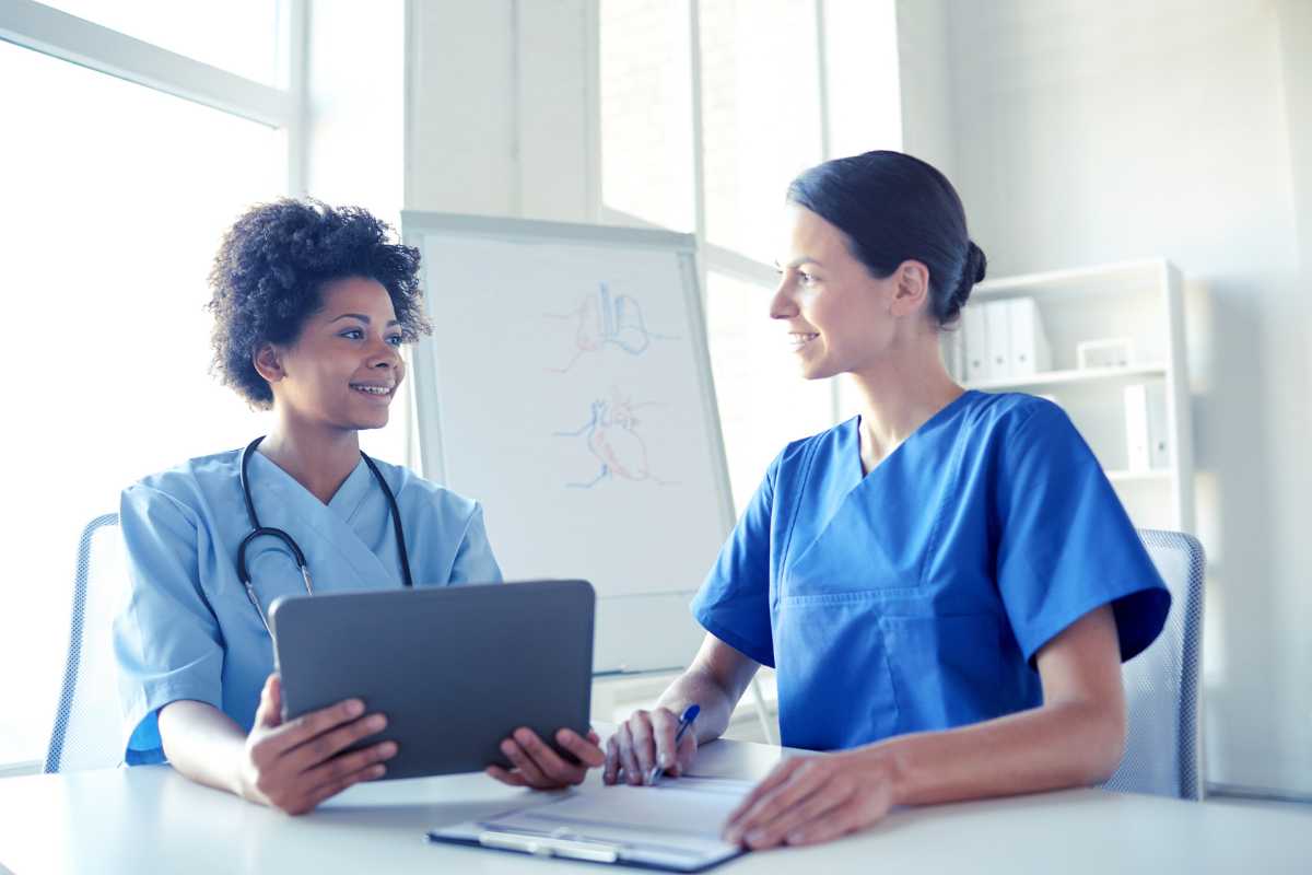 Two nurses sitting at table and looking at tablet during nursing professional development week.