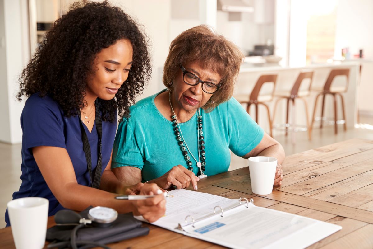 A nurse sits down and helps a nursing home resident file some paperwork.