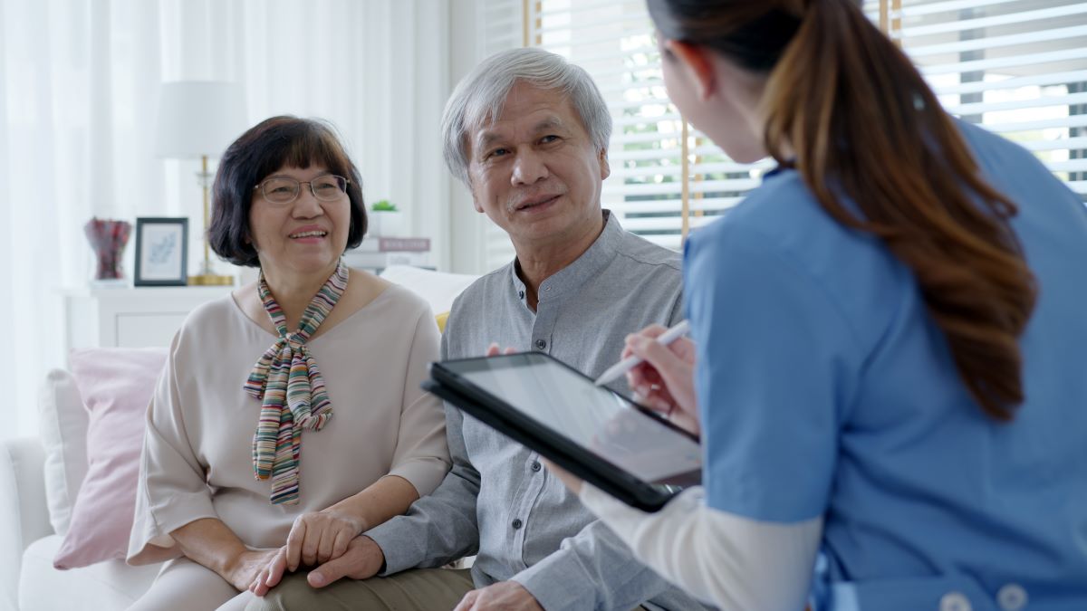 A nurse takes notes as she talks with an elderly couple at an assisted living facility.