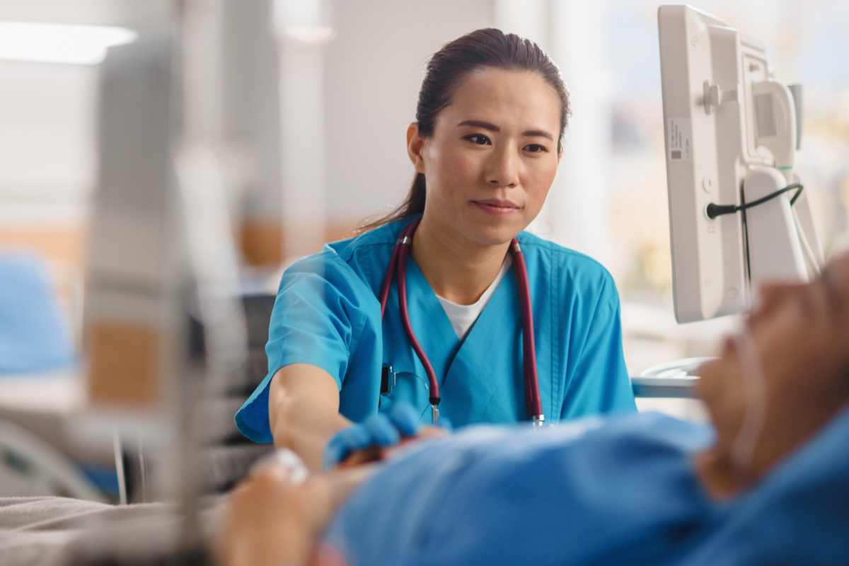 Palliative care nurse in scrubs at the bedside comforting an intubated patient.
