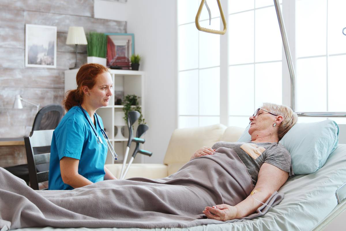A patient companion sits by a woman in a hospital bed.