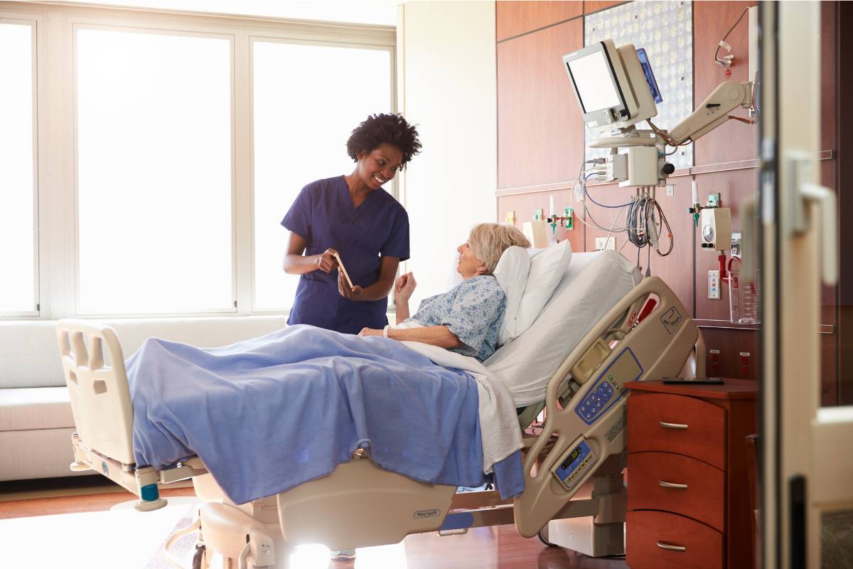 A nurse implements purposeful rounding with a patient in a hospital room.