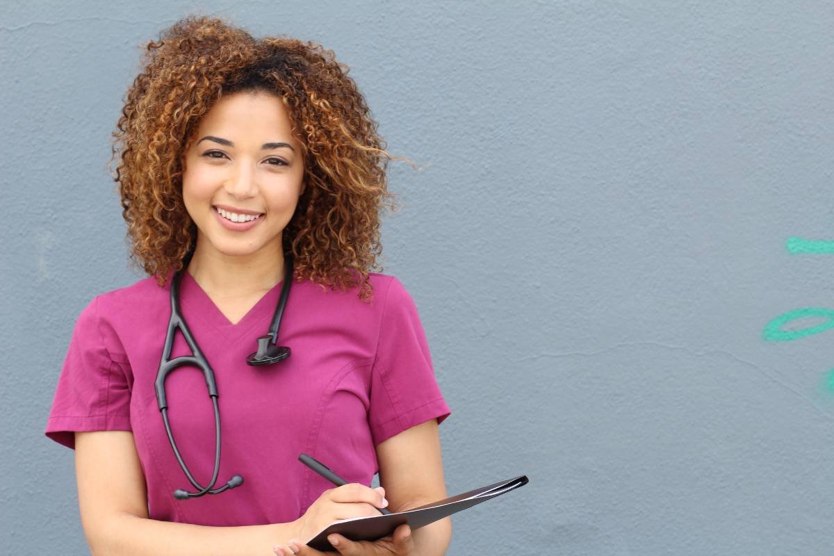 A nurse in pink scrubs prepares their school nurse cover letter.