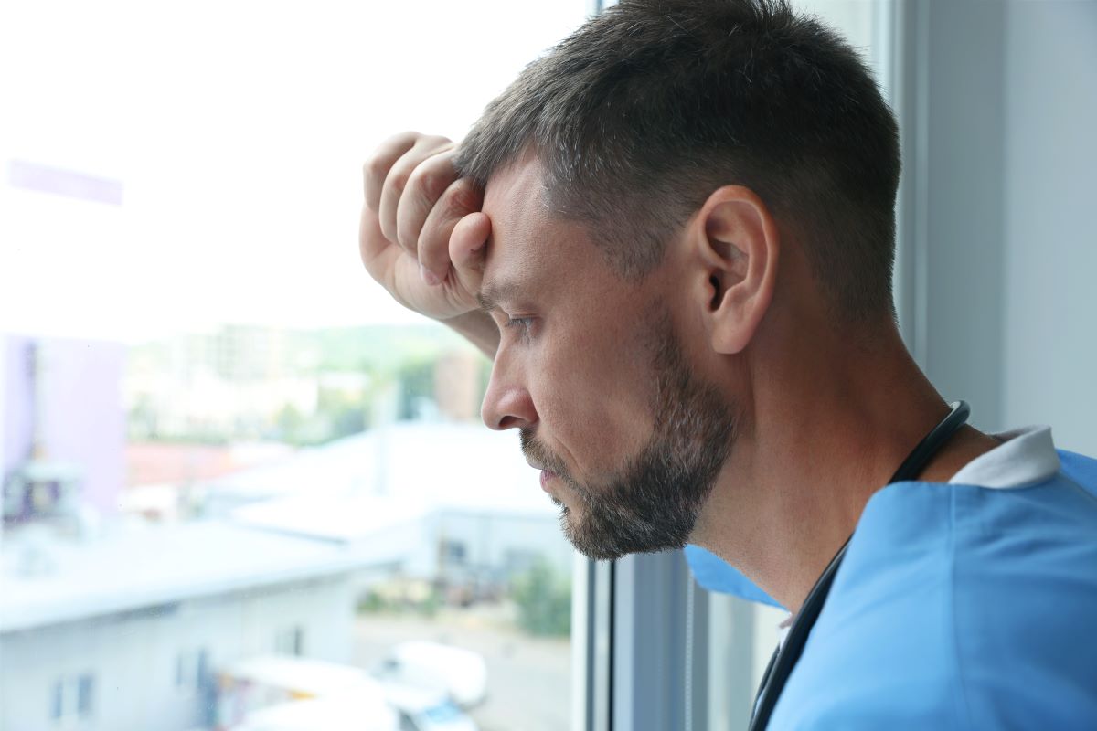 A stressed-out nurse takes a break from his shift and gazes out of a window.