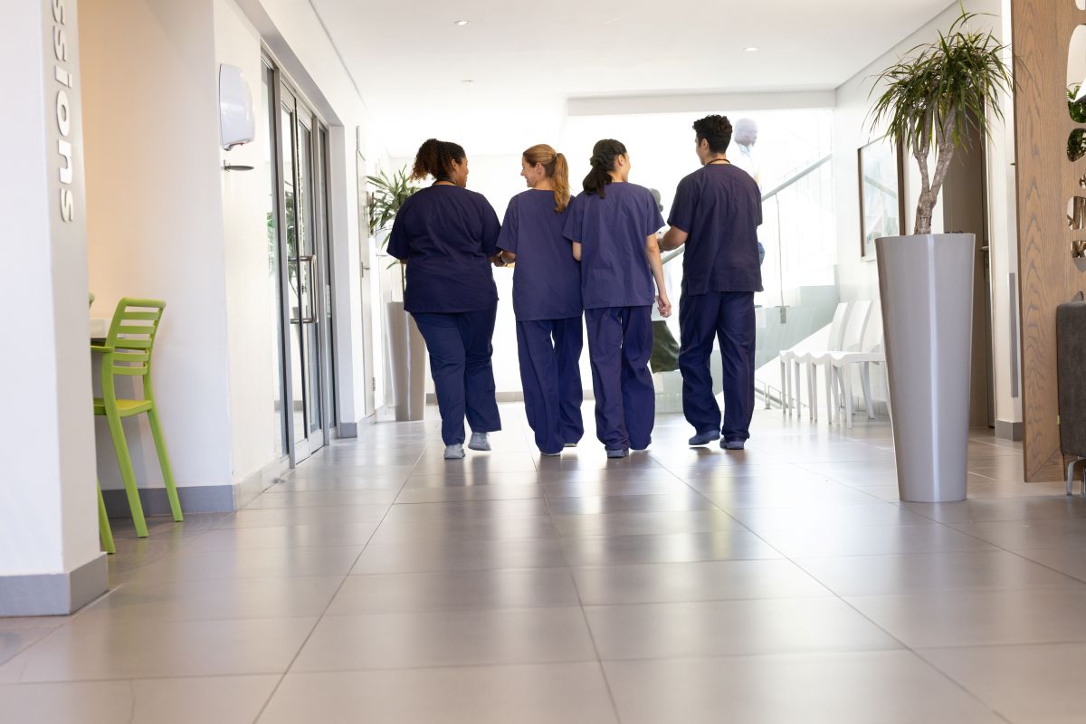 A group of four nurses walks down a hospital hallway.