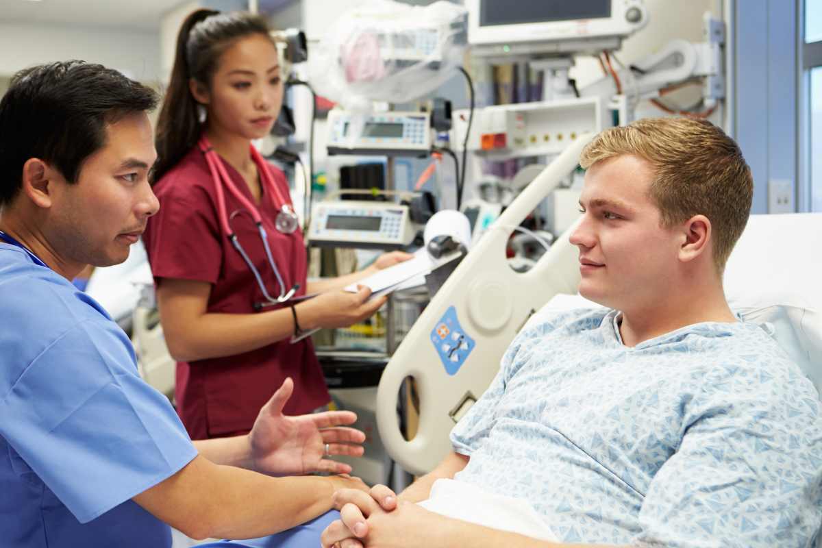 Trauma nurse talking with male patient in a hospital bed.