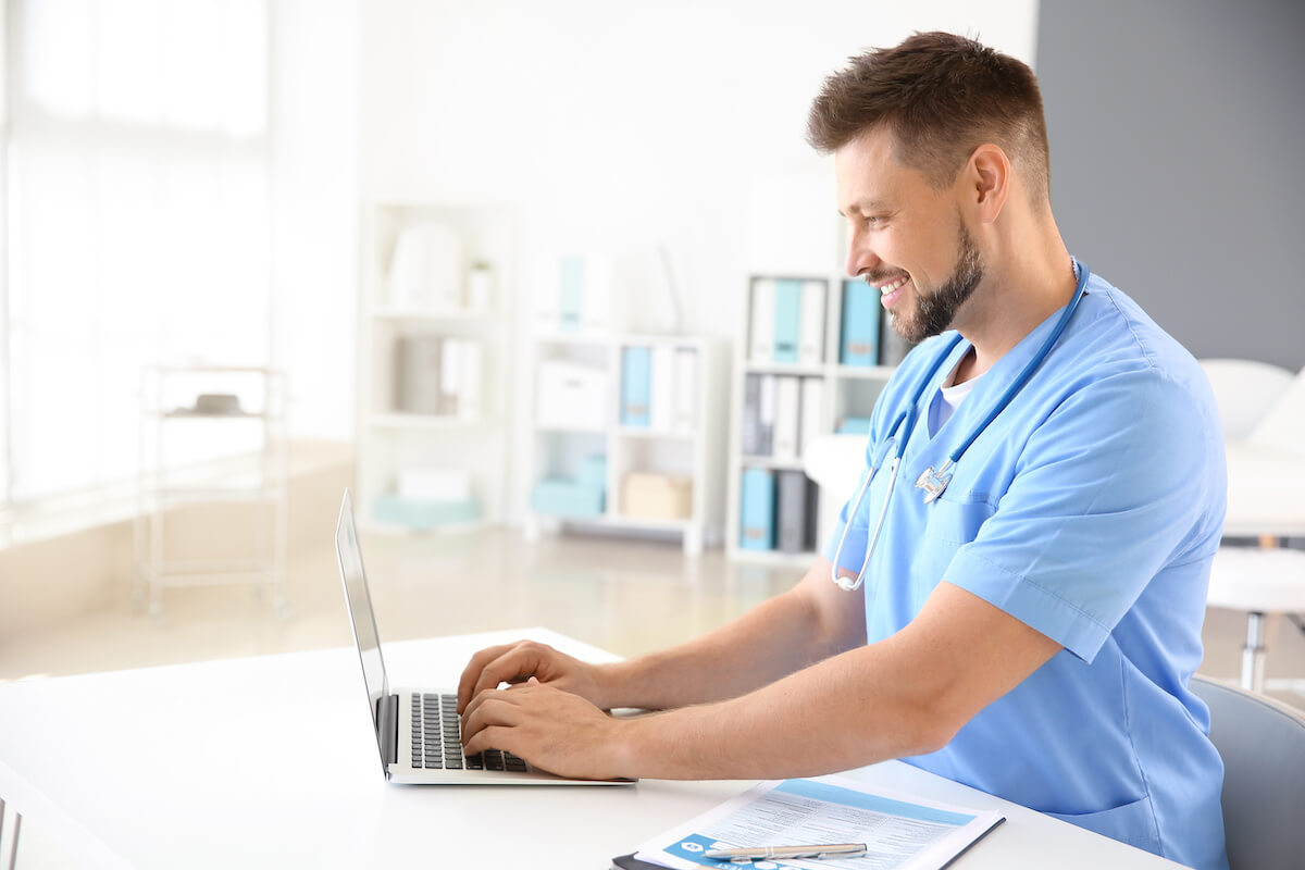 Male nurse sitting at desk and working on a laptop for continuing ed credits.