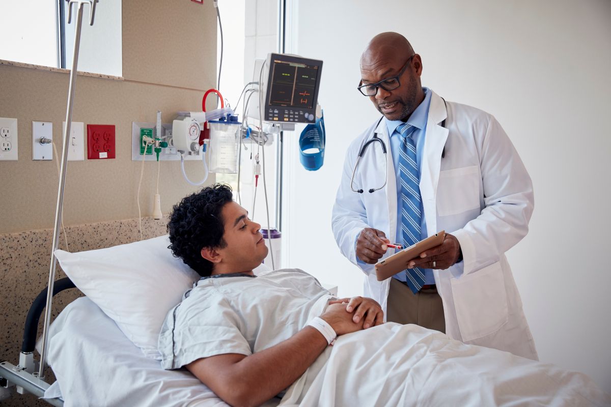 A physician speaks to one of his patients, who is in a hospital bed.
