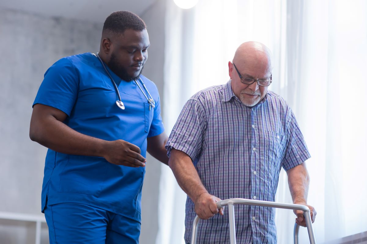 A nurse demonstrates the use of universal fall precautions as he assists a patient with a walker.