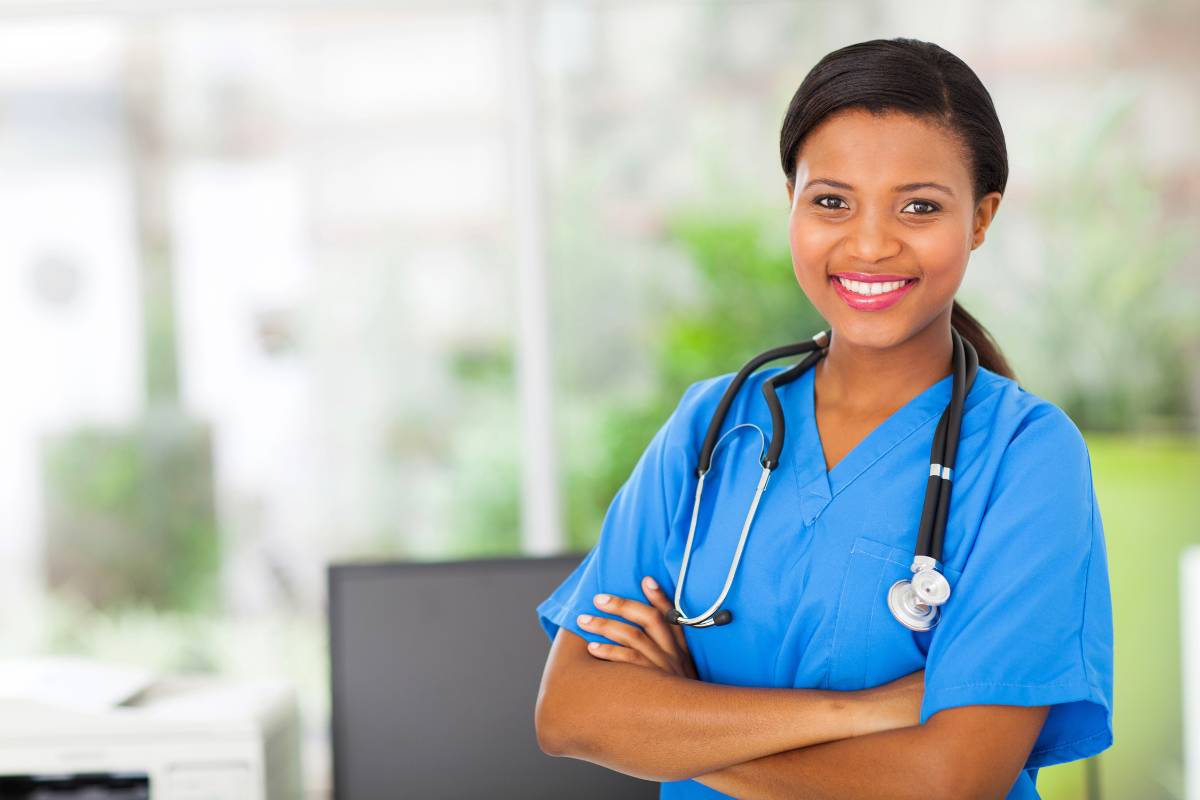 A nurse practitioner in blue scrubs with her arms folded and smiling