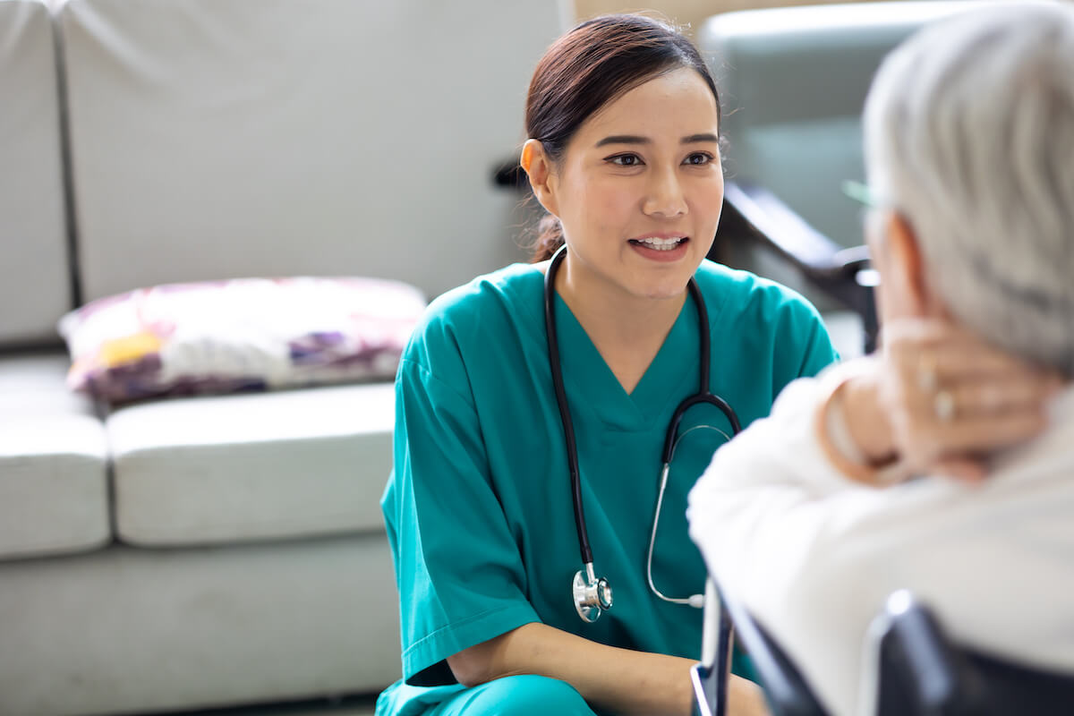 Young nurse assistant crouching and talking with elderly resident in a wheelchair.
