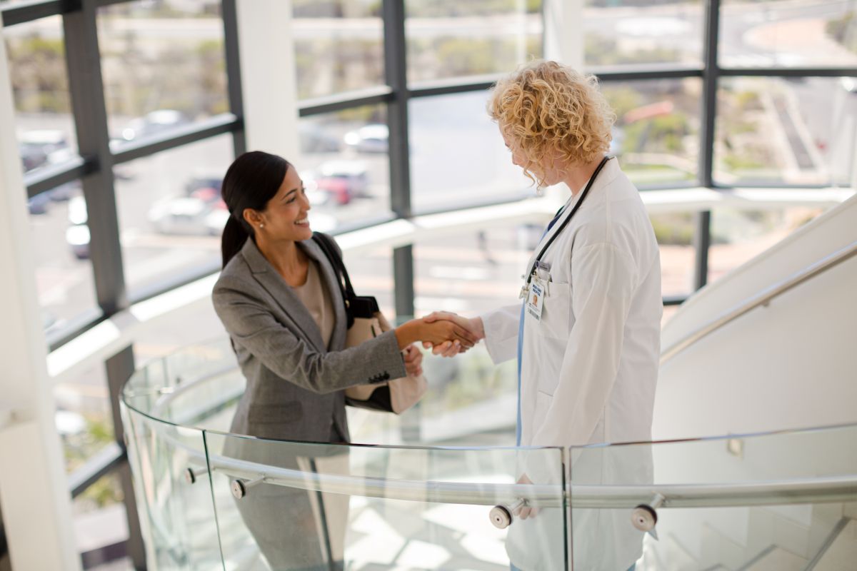 A hospital's CXO, walking up the stairs, meets with another member of the management team.