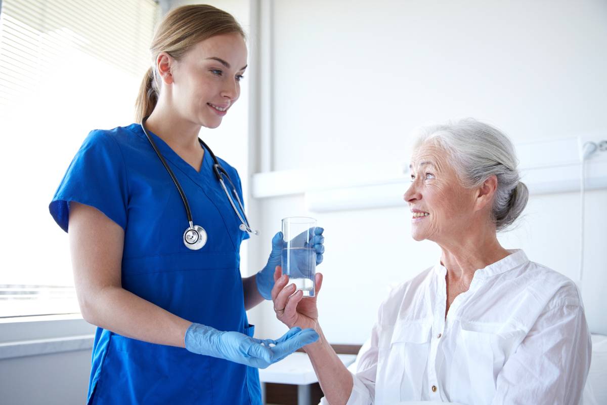 A nurse offers a patient her medication while answering the question, What is medication reconciliation?