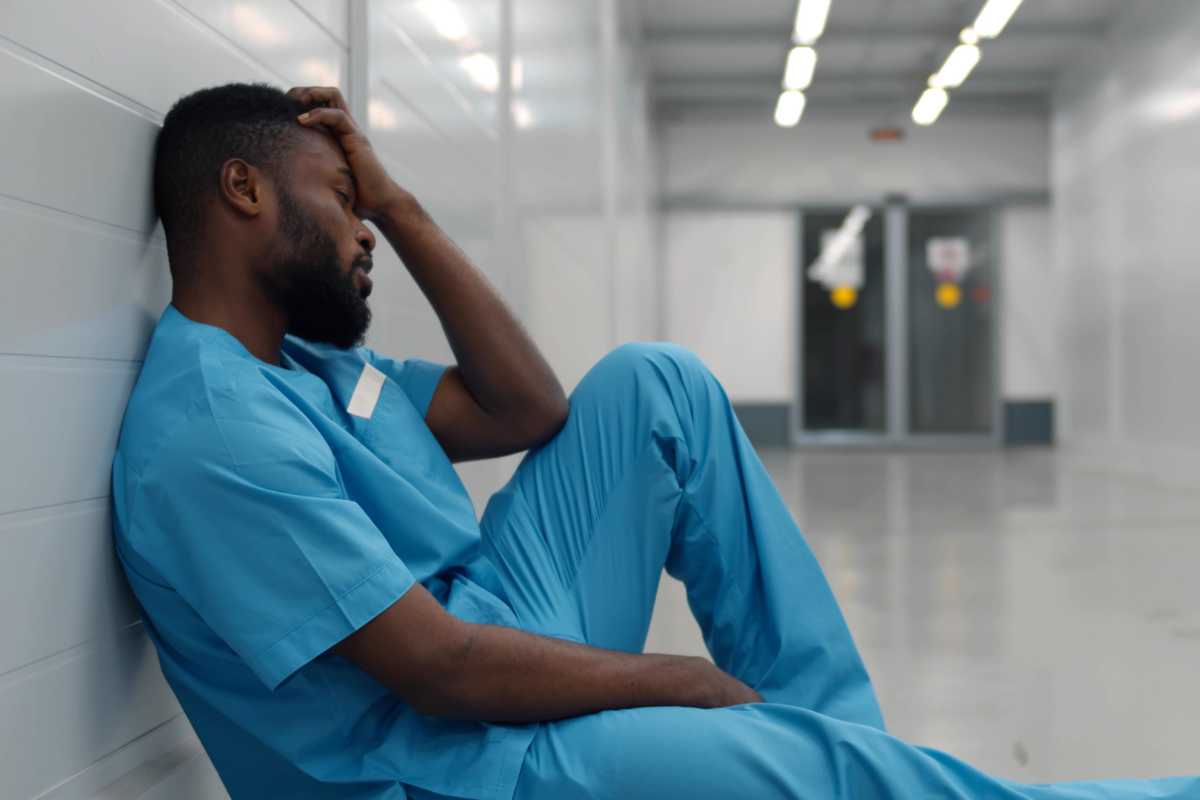 Tired nurse sitting in hallway contemplating quitting nursing.